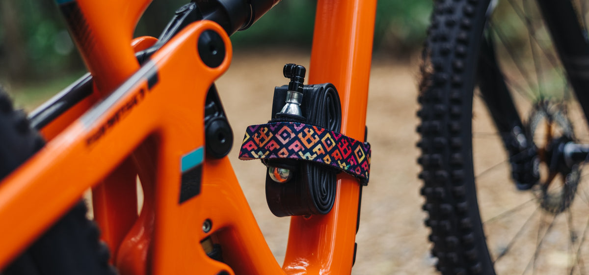 Granite Rockband+ in a colorful diamond pattern strapping a spare tube and CO2 inflator to an orange full-suspension frame