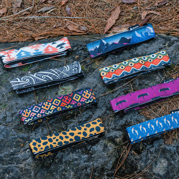 Eight Granite Rockband+ straps in printed patterns laid out on a mossy rock among pine needles