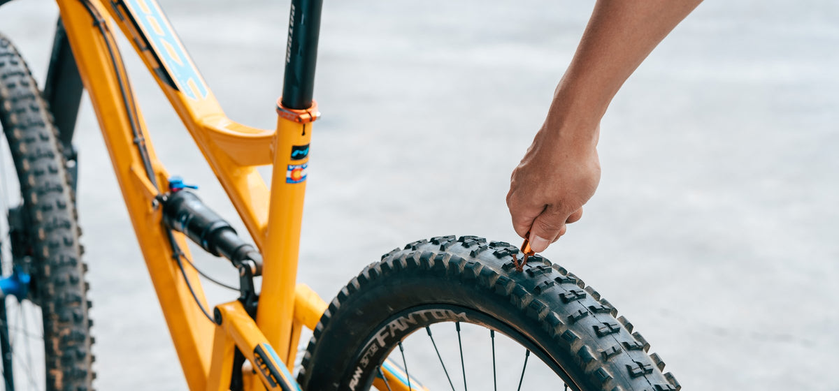 Hand pushing an orange Granite Suture Aero plug fork into the rear tire of a yellow mountain bike