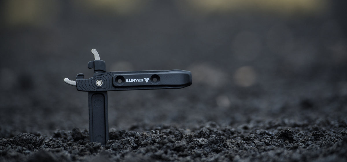 Black Granite Talon tire lever standing upright in dark soil, stainless steel tips at the top