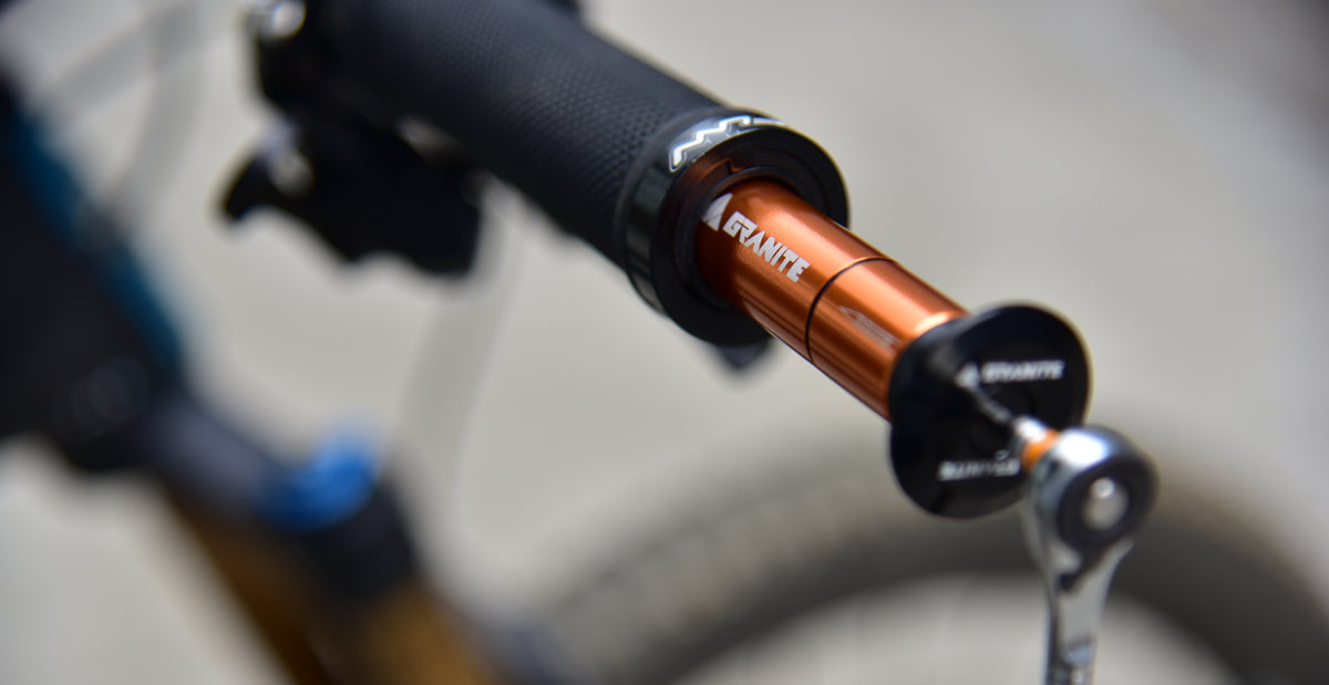 Orange Granite Stash tire plug kit stored in the end of a black mountain bike handlebar, bike blurred behind