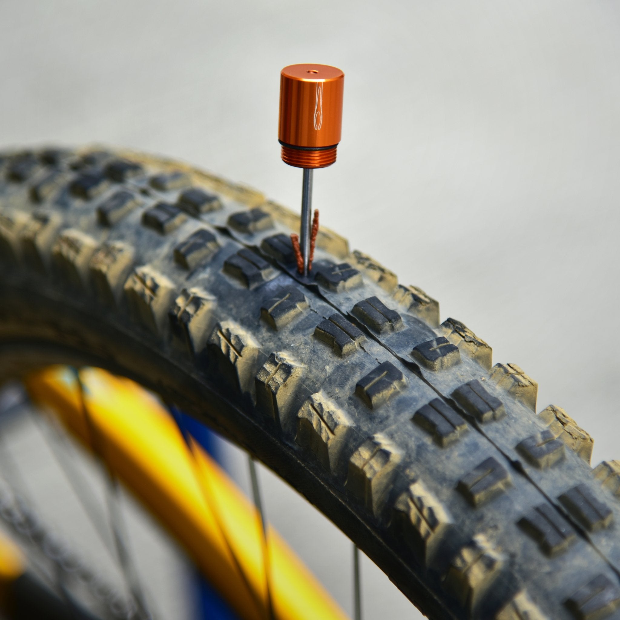 Close-up of a mountain bike tire showing a Granite Stash tire plug inserted into a punctured section of the tread.